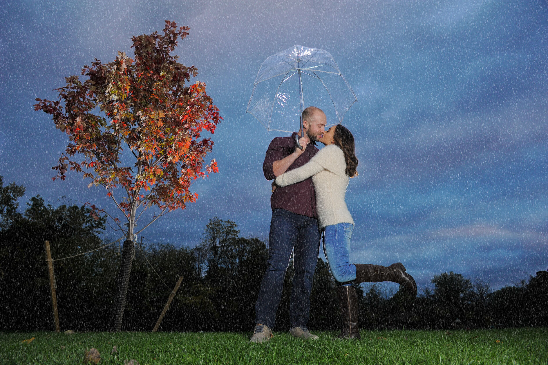 A newly engaged couple kissing in the drizzle as the sun sets on metro Detroit, Rochester park Michigan engagement session.