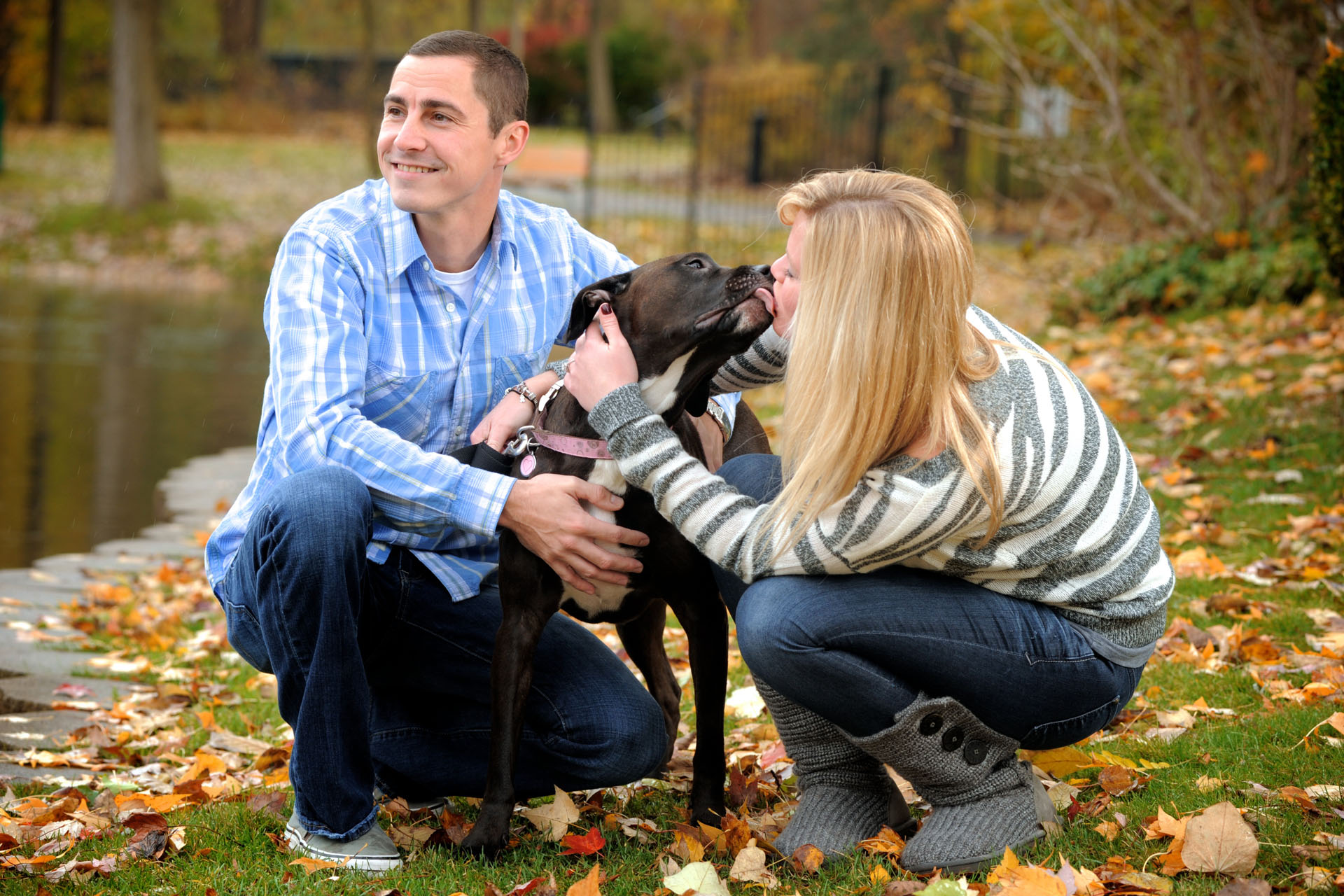 Hilarious engagement photographer takes fun, candid engagement portraits like this newly engaged couple with the bride to be getting a full on wet kiss from her dog while her fiancé looks away.