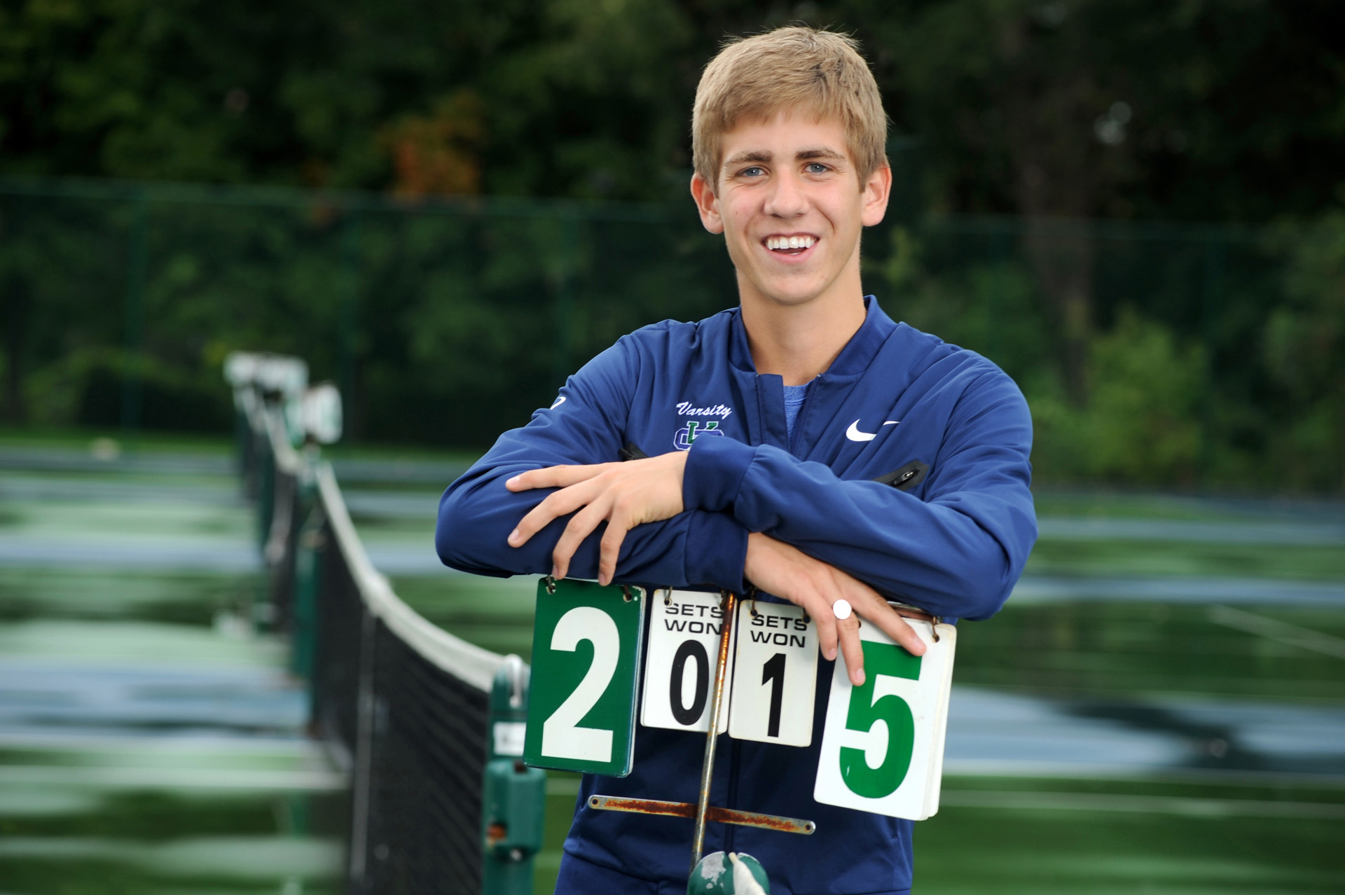 cranbrook, Michigan senior photographer's portrait of the high school senior posing for his senior pictures at Cranbrook School in Bloomfield, Michigan on their iconic blue tennis courts.