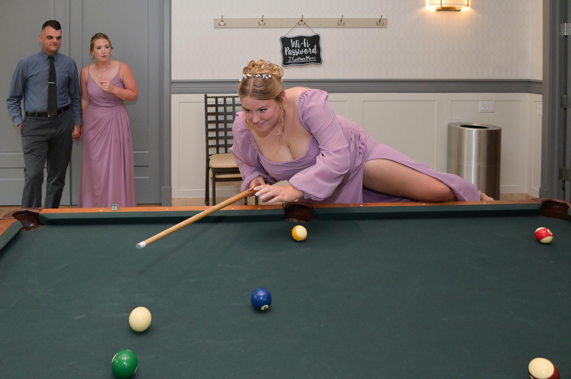 A bridesmaid climbs onto the pool table for the perfect shot during a wedding at 2 Gather More in Auburn Hills, Michigan.