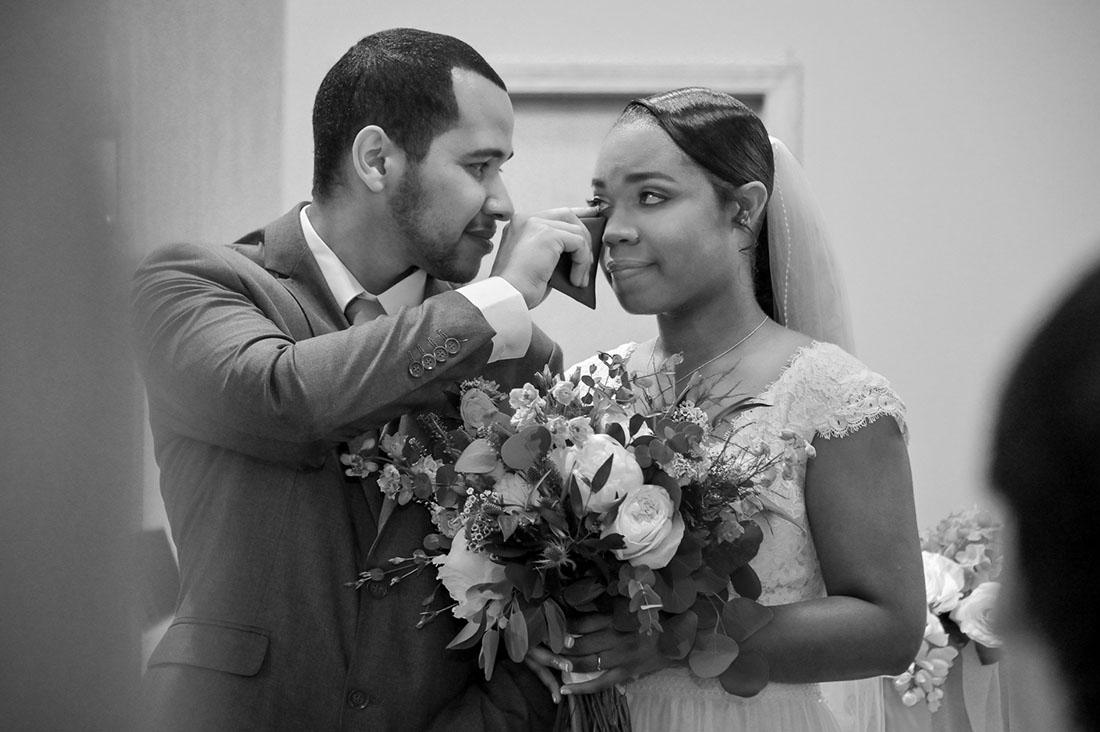 The groom wipes his wife's eyes as their friends sing to them during their wedding ceremony at Jesus-Baptist-Michigan-Church in Troy, Michigan.