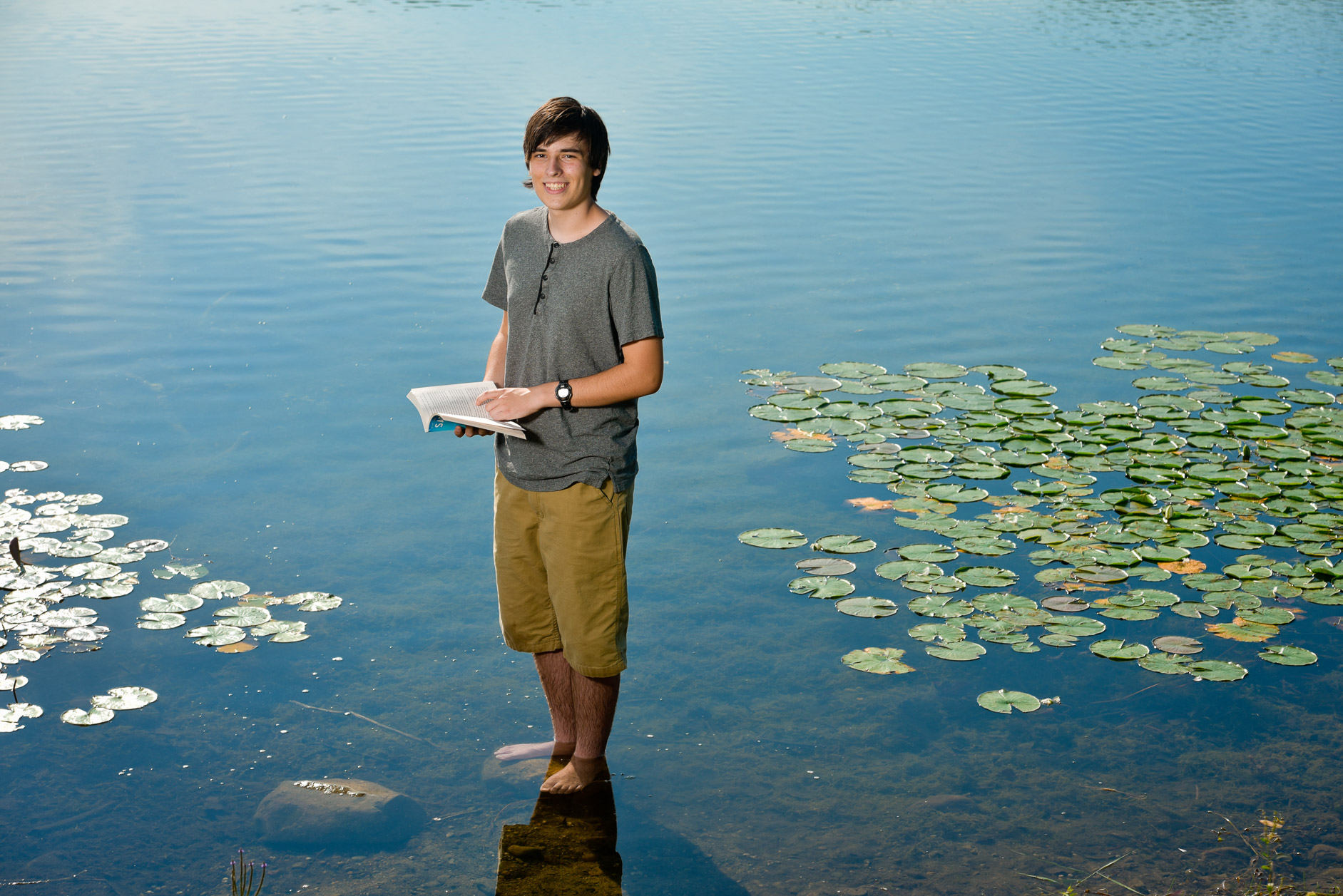 A Romeo high school senior stands in a lake reading his favorite book for his Oakland County senior photo.