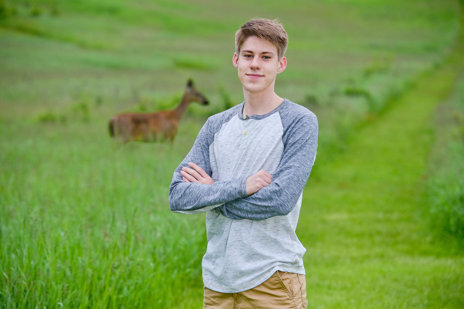 Senior posing for senior photo in rural areas of Troy, Michigan while a deer passes by.