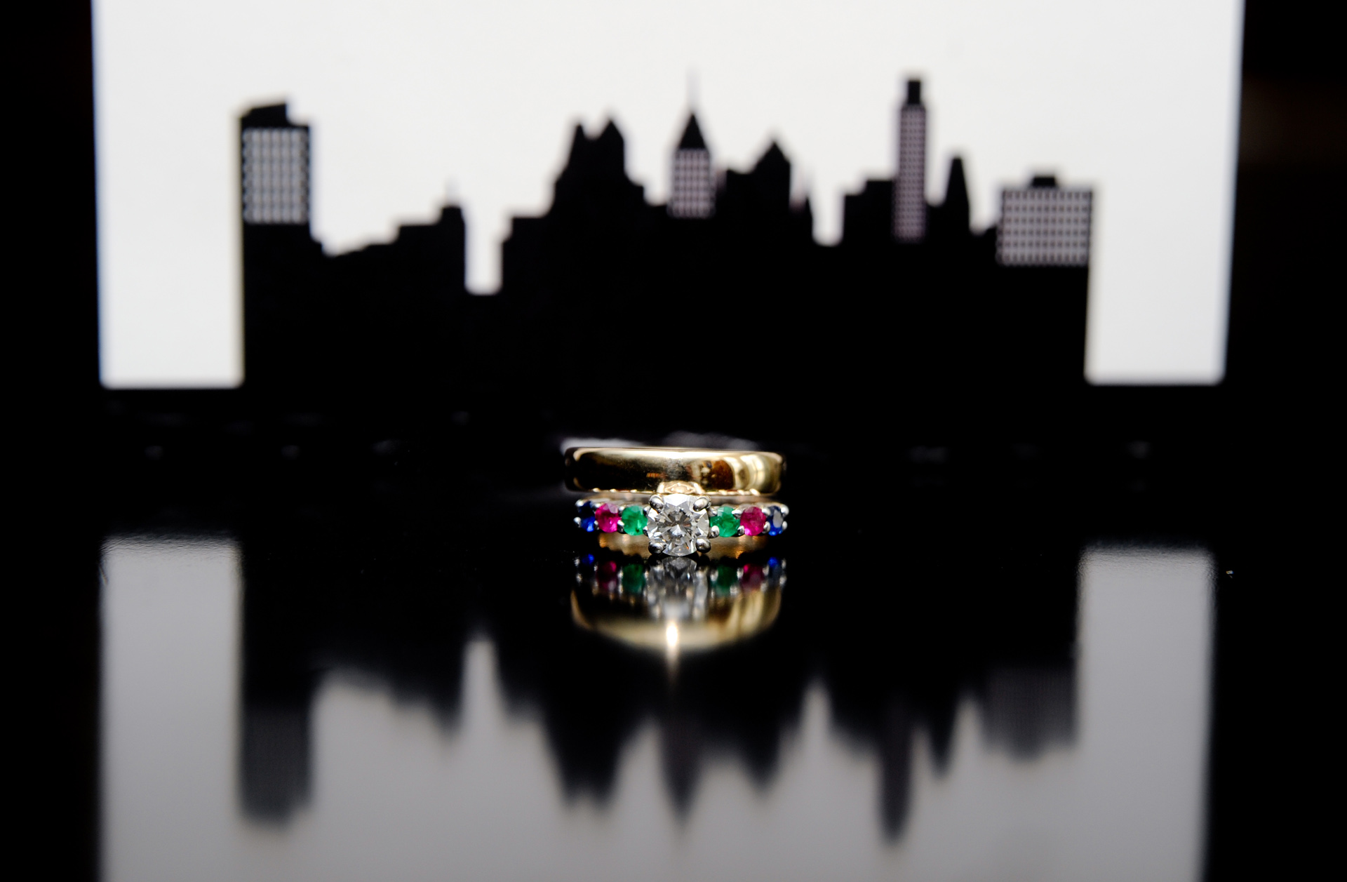 Groom and bride's rings sit in front of their super cool Detroit skyline invitation while it reflects on the glossy dresser at a Detroit, Michigan wedding.