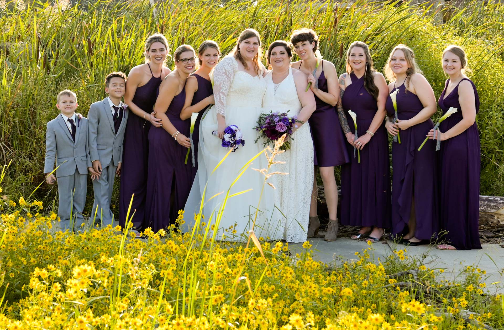 The brides pose with their bridal party at a park in Livonia, Michigan.