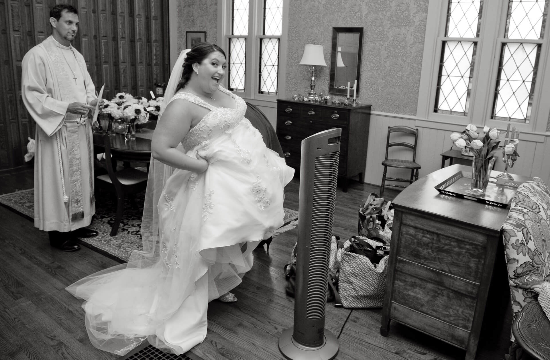 Bride hikes up her dress in Metro Detroit, Michigan to cool off just as the priest walks into the room.