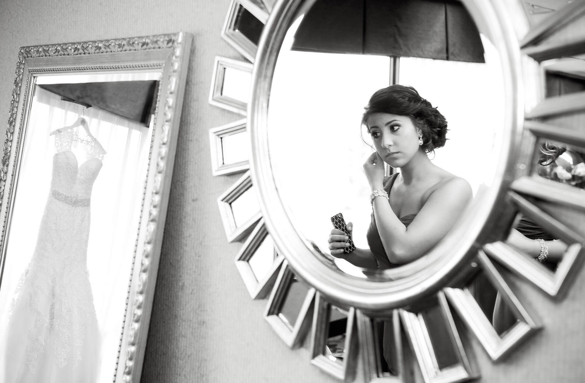 A bridesmaid gets ready in Rochester, Michigan at the hotel while the bride's dress hangs in the mirror taken by bride's favorite Michigan wedding photographer.
