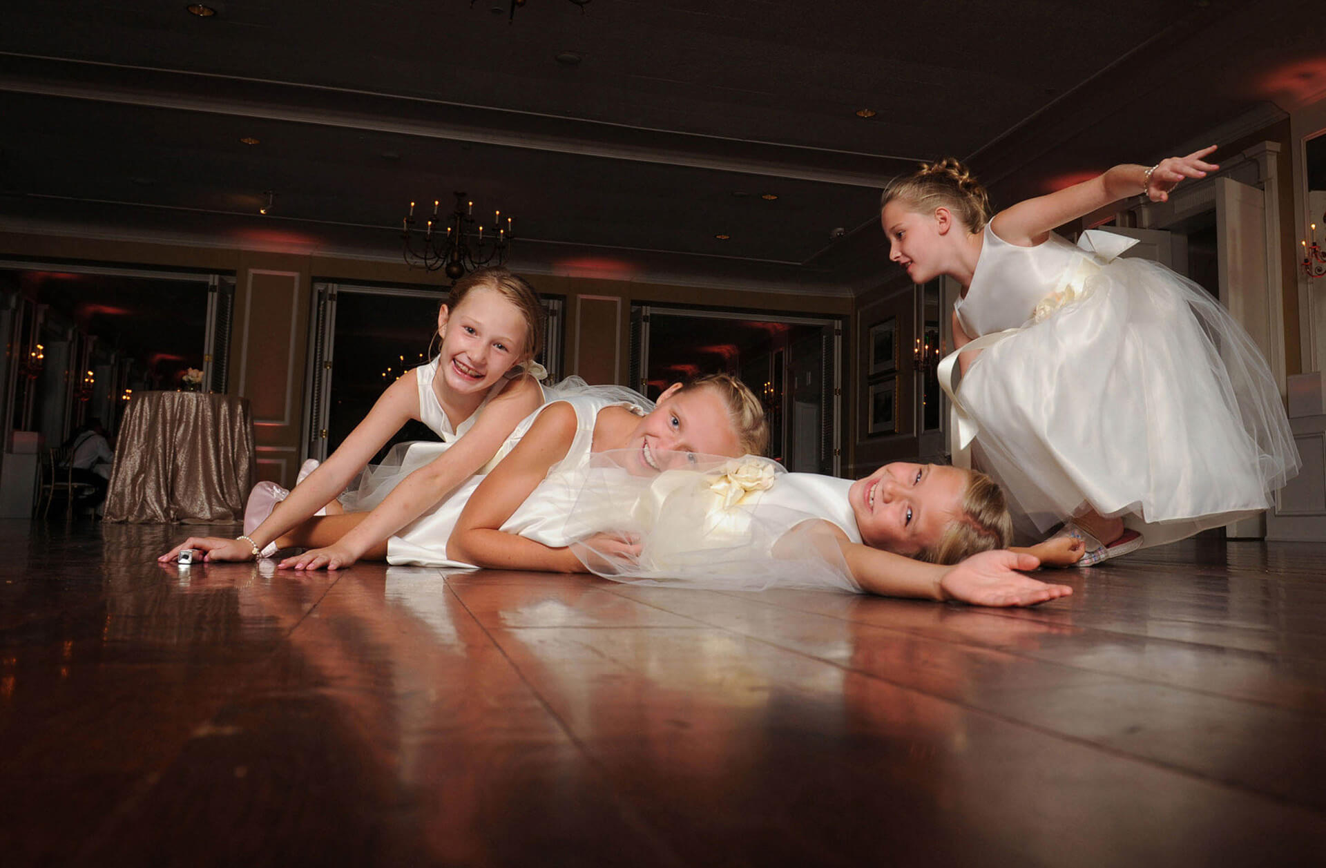 The flower girls have a spontaneous pile on in the middle of the dance floor at the Oakland Hills Country Club in Birmingham, Michigan wedding reception in this fun candid moment captured by one of the most affordable Michigan wedding photographers in Metro Detroit, Michigan.