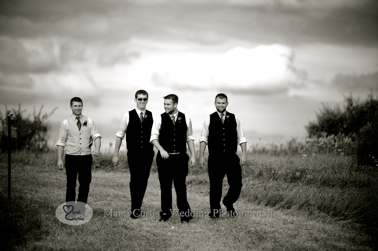 The groomsmen and the groom wander over the hill from a cornfield at an outdoors, country Michigan wedding.