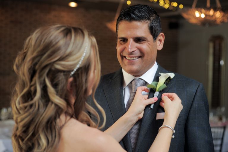 Bride pins the groom's boutonniere on him at their tiny second wedding at Cafe Cortina in Farmington Hills, Michigan.