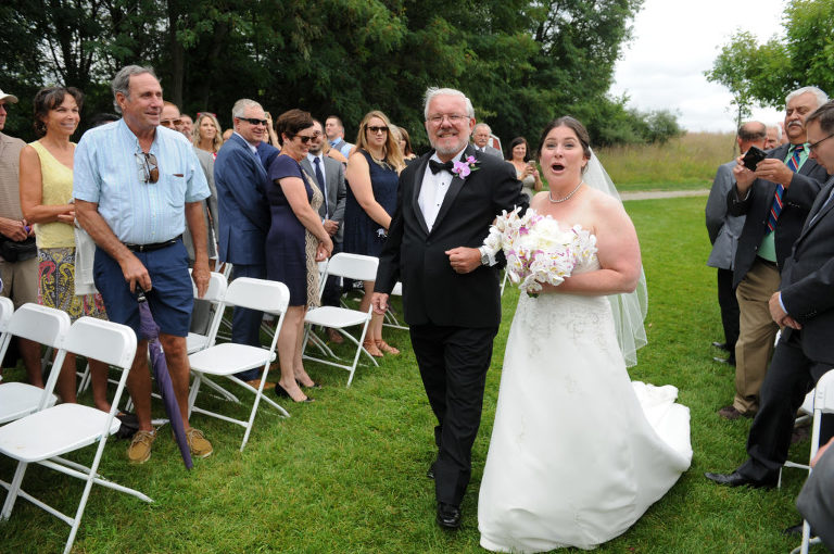 The bride and her father walk down the path to the ceremony site at the Indian Springs Metropark wedding in White Lake, Michigan as the bride spots her matron of honor crying at the end of the "aisle".