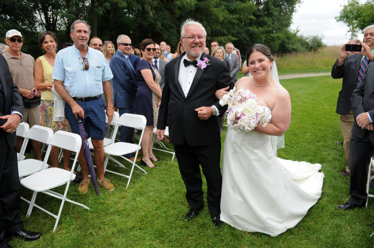 The bride and her father walk down the path to the ceremony site at the Indian Springs Metropark wedding in White Lake, Michigan.