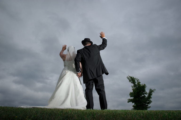 The bride and groom wave to their guests in the stormy looking weather after the wedding ceremony at the Indian Springs Metropark wedding in White Lake, Michigan.