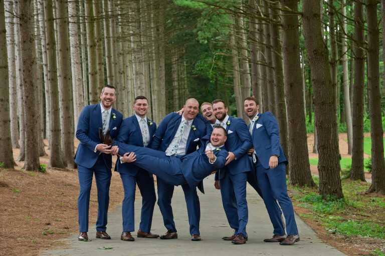 The groomsmen attempt to pick up the groom several times during this hilarious wedding party photo taken at Shepherd's Hollow's new wedding venue in Clarkston, Michigan.