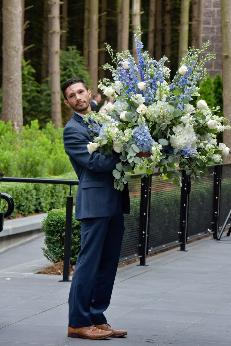 One of the guests helps to move a floral arrangement inside during the cocktail hour after wedding ceremony at Shepherd's Hollows Golf Club Clarkston, Michigan.