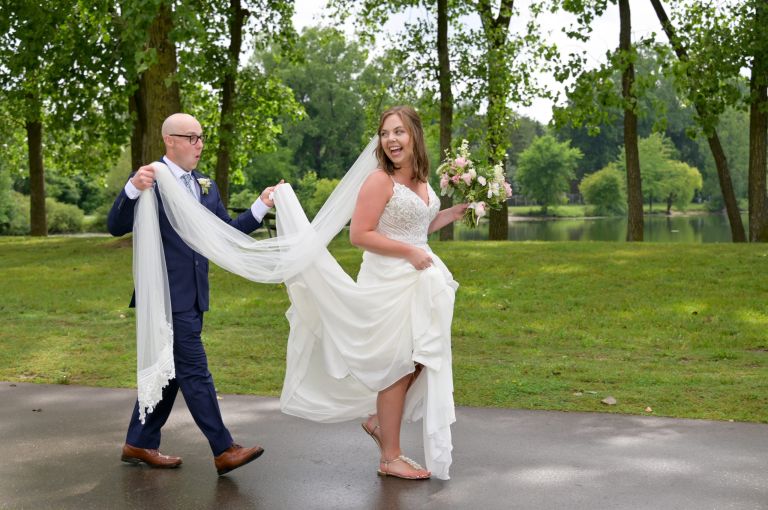A groom helps his bride with her wedding dress while out for photos.
