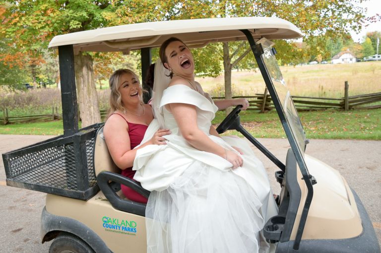 The bride laughs as she arrives on a golf cart for her fall wedding at Addison Oaks Buhl Estates in Leonard, Michigan.