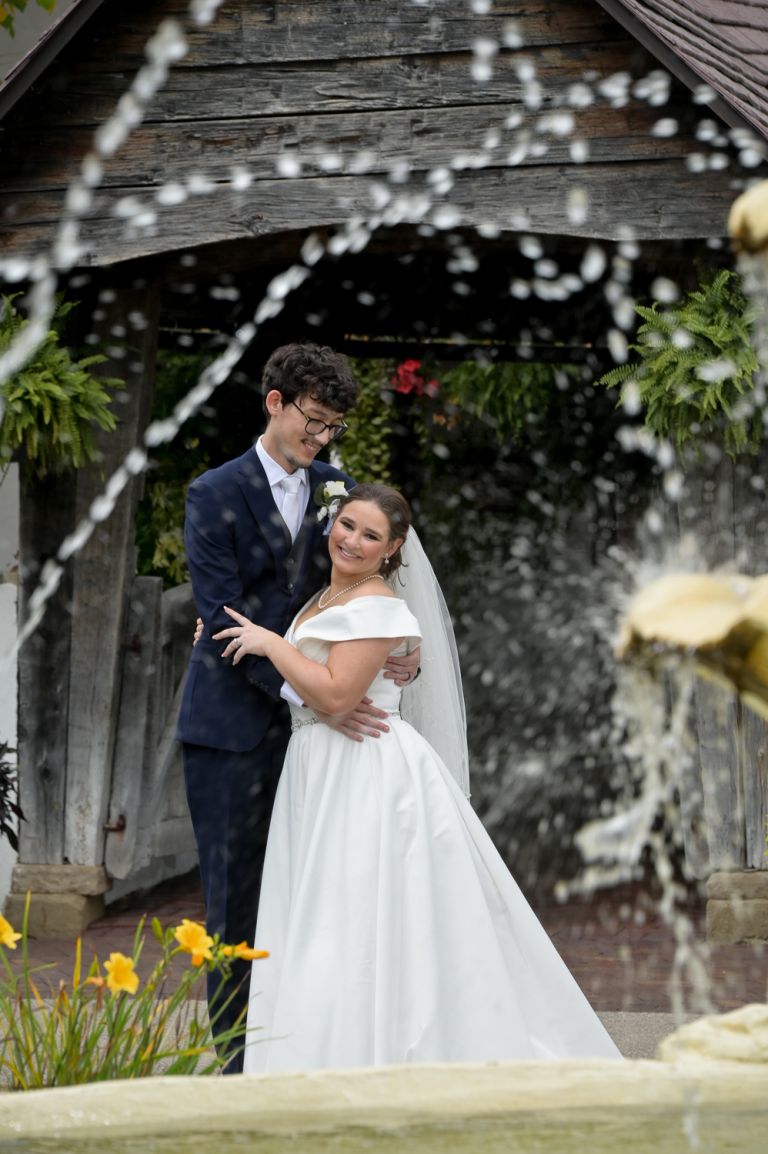 The bride and groom pose for photos at the fountain during their fall wedding at Addison Oaks Buhl Estates in Leonard, Michigan.