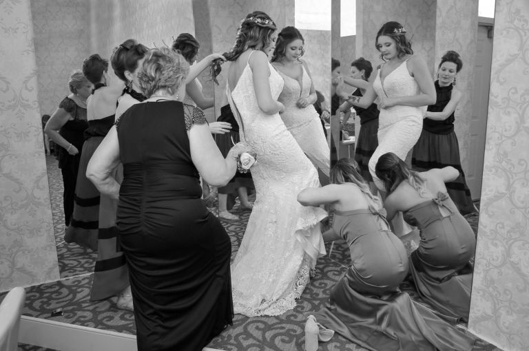 The bride gets lots of assistance getting into her dress and shoes.