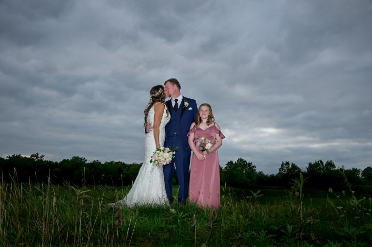 The bride, the groom and his daughter posing for photos on the golf course.