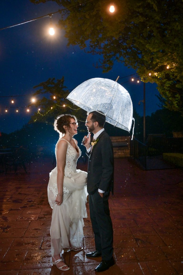 A couple playing in the rain at the end of their Pine Knob Mansion wedding.